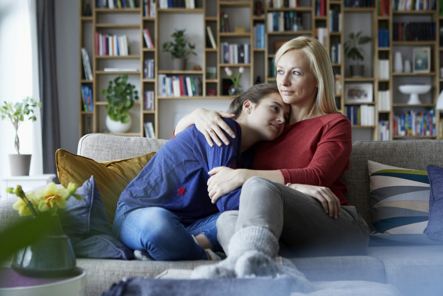 Mother and adolescent daughter sitting on couch with arms around